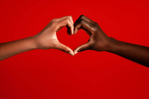 Two+multiracial+girls+making+heart+sign+against+red+background